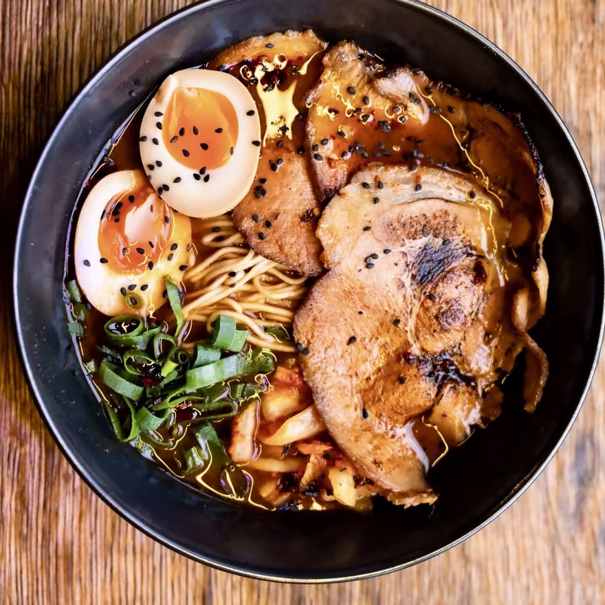 Ramen w ciemnej misce z jajkiem i plastrami karkówki, widok z góry